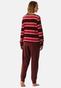Gestreiftes Loungewear-Set in bordeauxrot und rosa Tönen, gefertigt aus weichem Stoff. Das Oberteil hat lange Ärmel; die Hose ist weit geschnitten mit elastischem Bund.