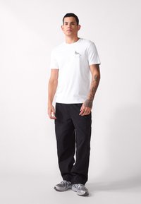 Camiseta blanca de algodón con un pequeño diseño gráfico en el pecho, combinada con pantalones cargo negros y zapatillas deportivas grises.
