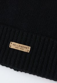Bonnet en tricot noir avec une texture côtelée et une étiquette en cuir beige portant un texte en relief "BELLEMERE NEW YORK." Fini lisse, matériau chaud.