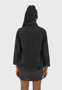 Černá džínová bunda s klasickým střihem, viditelným prošíváním a manžetami na knoflíky, s textilní nášivkou na horní části zad.