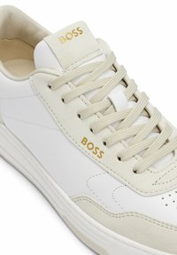 Weiße und beige Sneakers mit cremefarbenen Schnürsenkeln und goldenem "BOSS"-Logo auf der Zunge und der Seite, mit genähter Sohle und glattem Leder.