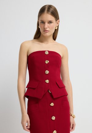 Crop top rosso senza spalline con design strutturato, dettagli in bottone dorato e due tasche frontali. Tessuto liscio, vestibilità su misura e stile formale.