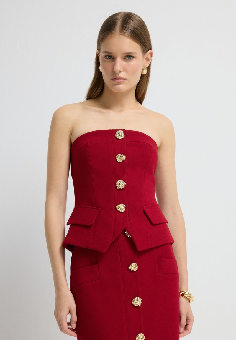 Rotes tailloses Oberteil mit strukturiertem Design, goldenen Knopf-Akzenten und zwei frontalen Taschen. Glatte Textur, maßgeschneiderte Passform und formeller Stil.