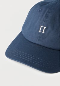 Μπλε σκούρο μπλε καπέλο του μπέιζμπολ με λευκό ρωμαϊκό αριθμό ΙΙ κεντημένο μπροστά, που δείχνει λεπτομερή ραφή στην γείσο και τα πάνελ.