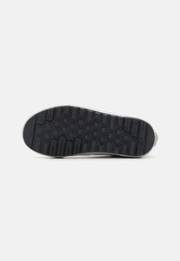 Suela de zapato de goma negra con patrones de tracción hexagonales y lineales. El borde presenta un contorno blanco liso y una ligera curvatura.