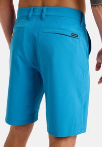 Blue swim shorts made of lightweight fabric; features pockets, a back flap pocket with emblem, and a tailored cut. Smooth texture throughout.