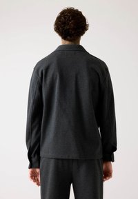 Giacca grigia scura, non strutturata, con una texture morbida. Presenta un colletto e polsini con bottoni. Design semplice con una vestibilità comoda.