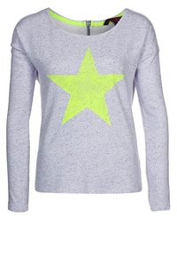 Camisa de manga larga hecha de tejido de punto gris claro, con un gran diseño de estrella amarilla neón en la parte delantera y un cierre de cremallera en la parte posterior.