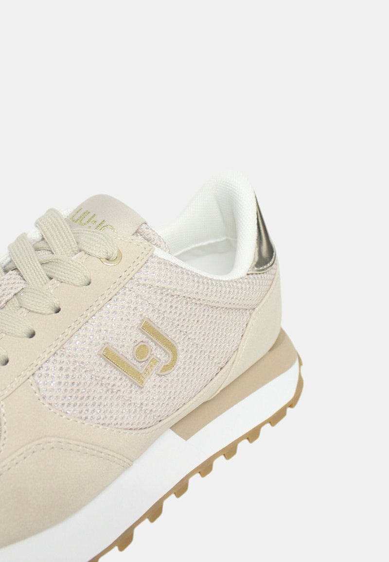 Scarpa sportiva beige con tomaia in rete, logo dorato e accento argento sul tallone. Caratterizzata da lacci rotondi e suola in gomma testurizzata.