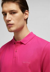 Roze polo shirt met een kraag, textuurstof, twee knopen en geborduurd "HECHTER" logo op de linkerkant van de borst.