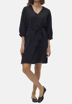 Robe noire en tissu léger, avec un décolleté en V, des manches bouffantes 3/4, une ceinture à la taille et une coupe décontractée. Portée avec des ballerines noires.