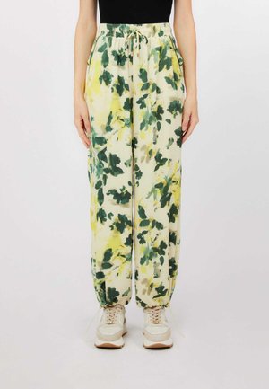 Donna che indossa pantaloni larghi a vita alta con stampa floreale verde e gialla, caviglie elastiche e sneaker beige.