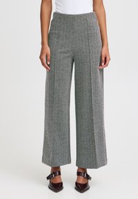 Weite Hosen aus diagonalförmigem Gewebe in Grautönen. Mit einem elastischen Taillenbund und glatter Textur. Braune Absatzschuhe sind sichtbar.