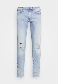 Pantalones vaqueros de mezclilla azul claro con un ajuste slim, que presentan áreas desgastadas y un ligero desvanecimiento. Incluyen cinco bolsillos y un cierre frontal con botón.