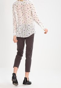 Blusa bianca trasparente con stampa di farfalle e fiori multicolore, abbinata a pantaloni slim-fit grigio scuro e stivaletti neri alla caviglia.