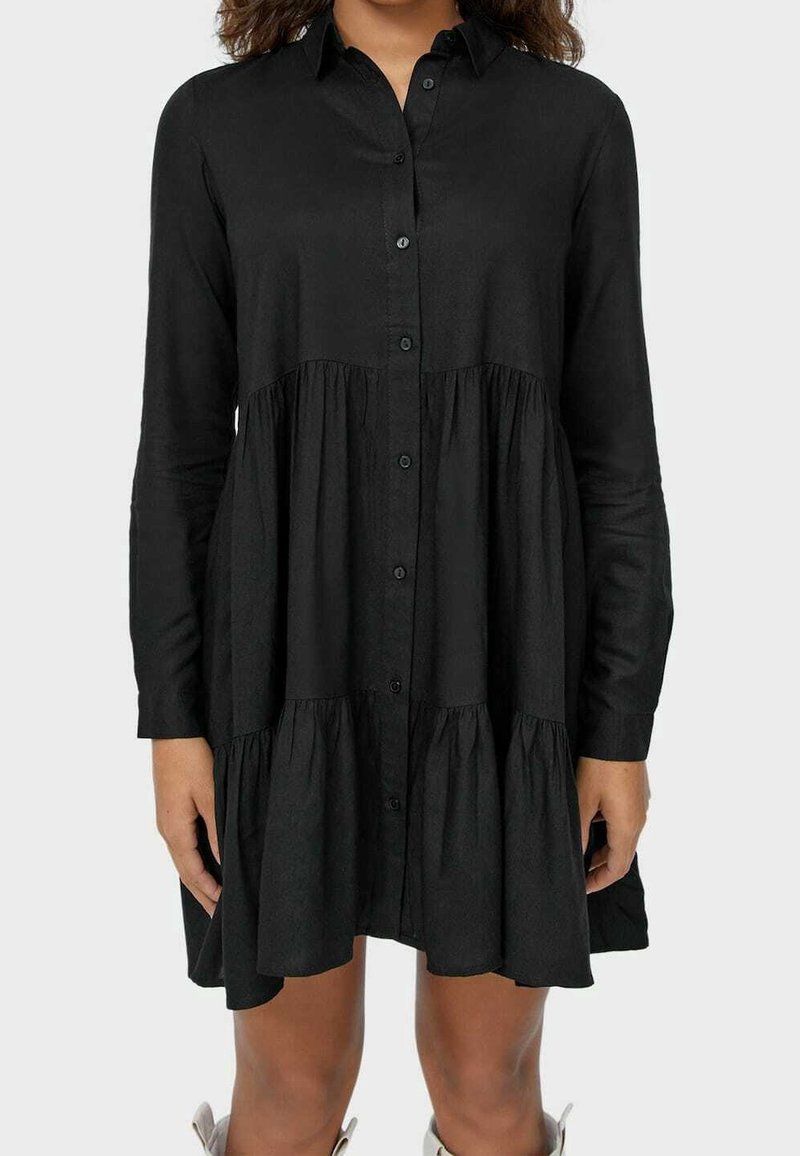 Svart, långärmad skjortklänning gjord av lätt tyg, med knapprad fram och flerfaldiga volanger vid fållen.