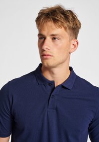 Marinblå polo skjorta tillverkad av texturerad väv, med krage, två svarta knappar och korta ärmar.