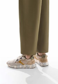 Sneaker in suede beige con finitura testurizzata, con accenti gialli e la scritta "VOILE BLANC" stampata sul tallone e sul lato, abbinate a pantaloni oliva.