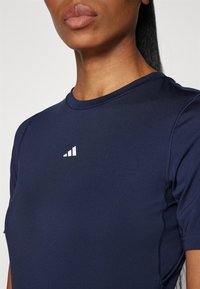 Laivastonsininen lyhythihainen urheilupaita pyöreällä kaula-aukolla ja valkoisella logolla rinnassa, jossa on sileä kangas ja litteät saumat.