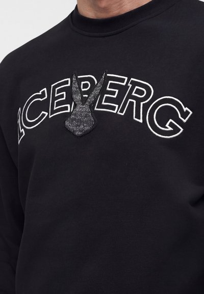 Μαύρο φούτερ με λευκό περίγραμμα κειμένου "ICEBERG" και υφασμάτινο μαύρο μοτίβο κεφαλής λαγού που αντικαθιστά το γράμμα "B" στο στήθος.