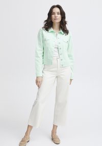 Chaqueta de mezclilla verde menta con dos bolsillos en el pecho y cierre de botones, combinada con pantalones cortos blancos y mocasines beige. Textura suave.