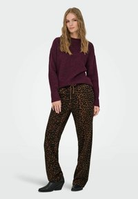 Burgunderfarbener Strickpullover mit langen Ärmeln, kombiniert mit braunen, leopardenmusternden, weiten Hosen und schwarzen, hohen Stiefeletten.