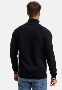 Pull en tricot noir avec un col haut, des poignets côtelés et une texture unie. Présente des rayures contrastantes au niveau de l'ourlet et des poignets.