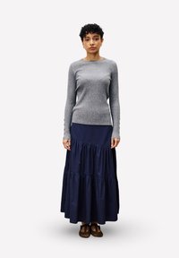 Graues, geripptes Langarmoberteil mit Knöpfen an den Ärmelbündchen, kombiniert mit einem marineblauen, gestuften Maxirock aus weichem Material, getragen mit braunen flachen Schuhen.