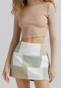 Hnědý žebrovaný rolák s dlouhými rukávy, kombinovaný s vícebarevnou mini sukní z kordu s patchworkem v zelené, béžové a bílé barvě.