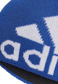 Beanie lavorato a maglia blu con logo bianco, costruzione senza cuciture e superficie a coste. Il bordo inferiore è rinforzato con cuciture nere.