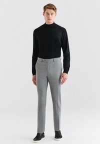Czarny sweter z półgolfem zestawiony z jasnoszarymi spodniami w kant o subtelnym wzorze w kratę, dopełniony czarnymi sneakersami.