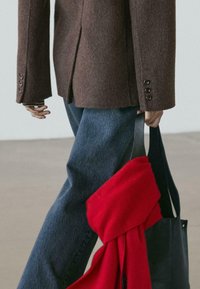 Brun uldbazelet med knapdetaljer, kombineret med blå denimjeans. Et rødt tørklæde ligger over en sort lædertaske.