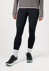 Mustad musta värvi sportlikud leggingud, millel on keha jäljendav disain, valmistatud siledast kangast. Neil on kontrastsed paneelid ja minimaalne logodetail.