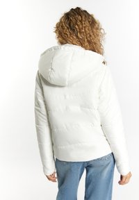 Hvid pufferjakke med hætte, der har en quiltet design, glat tekstur og elastiske manchetter, parret med blå jeans.