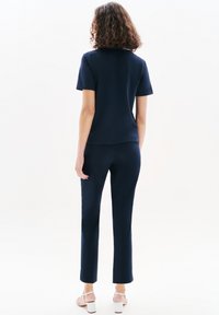 Granatowa bluzka z krótkim rękawem i okrągłym dekoltem, w zestawieniu z dopasowanymi spodniami, wykonana z gładkiego materiału, pokazana od tyłu.