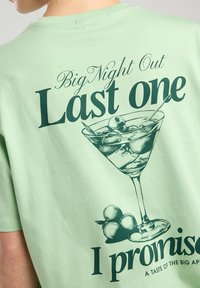 Mint green cotton t-shirt featuring a graphic of a cocktail glass with olives, and the text "Big Night Out Last one I promise" in dark green.