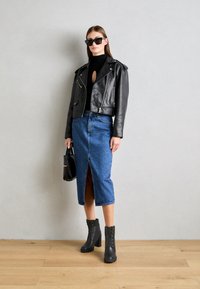 Veste moto en cuir noir, col roulé noir ajusté, jupe midi en denim avec fente à l'avant, bottines noires et lunettes de soleil noires oversize.