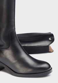 Bota de tobillo de cuero negro con un acabado suave, tacón ligero y punta redondeada. Incluye una bolsa de polvo negra en el fondo.
