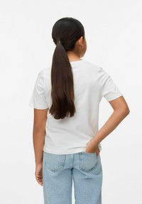 Camiseta de algodón blanca de manga corta y cuello redondo, combinada con unos vaqueros de denim de pierna ancha de color azul claro, vista desde atrás.