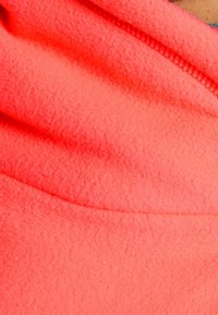 Tejido de forro polar en un brillante color coral, con una textura suave. El diseño incluye un escote redondeado y detalles de costura sutiles.