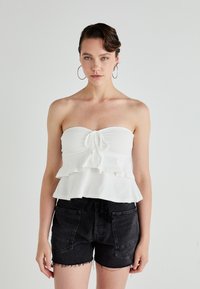 Witte strapless top met gerimpelde lagen en een trekkoord aan de voorkant. Gecombineerd met zwarte denim shorts met een rafelrand en zijzakken.