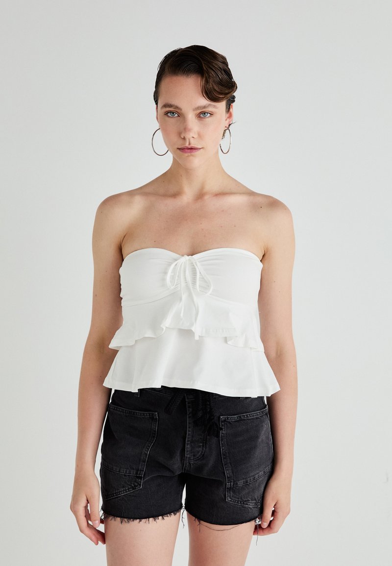 Witte strapless top met gerimpelde lagen en een trekkoord aan de voorkant. Gecombineerd met zwarte denim shorts met een rafelrand en zijzakken.