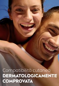 Due persone sorridono vicine, con texture della pelle visibili. Uno ha un tatuaggio sul braccio; lo sfondo è blu. Sotto c'è del testo con dichiarazioni sul prodotto.