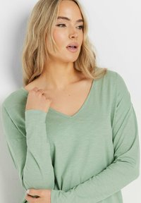 Langarm-T-Shirt mit V-Ausschnitt in Hellgrün. Leichtes, strukturiertes Material mit subtilen Variationen. Mit einem entspannten Schnitt und sanft abgerundeten Säumen.