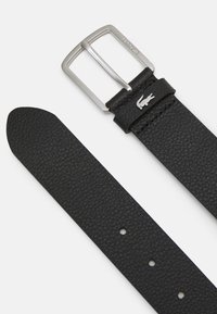 Black textured leather belt with a shiny silver metal buckle, featuring a small logo accent and punch holes for adjustment.