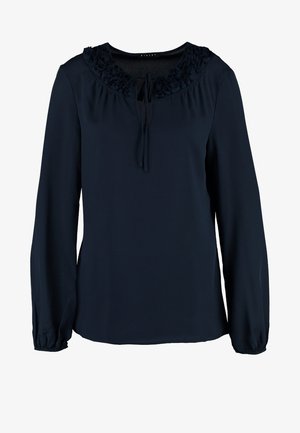 Námořnická blůza se sešitým výstřihem a detailem na zavázání, kterou modelka kombinovala s bílými úzkými džíny a hnědými kotníkovými botami. Modelka nese kovovou kabelku.