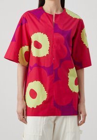 Rød bomuldsbluse med store gule og lilla blomster mønstre, korte ærmer og rund halsudskæring. Har en frontstolpe.