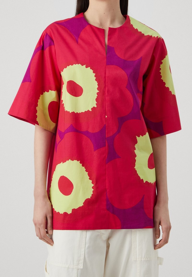 Rød bomuldsbluse med store gule og lilla blomster mønstre, korte ærmer og rund halsudskæring. Har en frontstolpe.