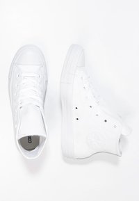 Ett par vita hög-top sneakers, en som visar toppvy med snörning, den andra i sidovyn som visar stjärnlogotypen på vristen.
