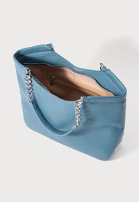 Bolsa tote em couro azul com superfície texturizada, detalhes em corrente prateada e fecho com zíper no topo. O interior possui um forro claro e um bolso com zíper.